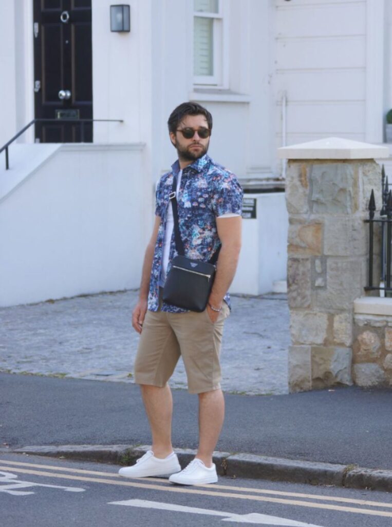 Man wearing a flower pattern shirt over a white t-shirt, beige chino shorts and white trainers.